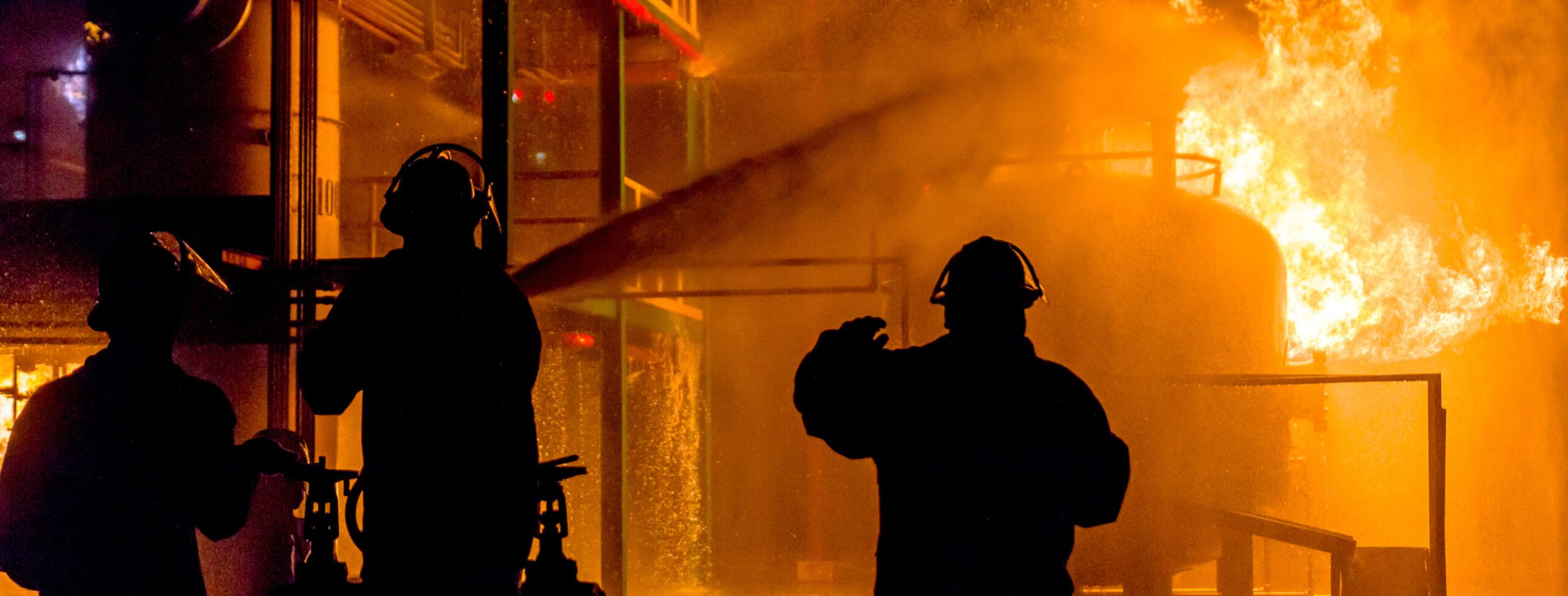 Firemen using water from hose for fire fighting at firefight training of insurance group. Firefighter wearing a fire suit for safety under the danger case.