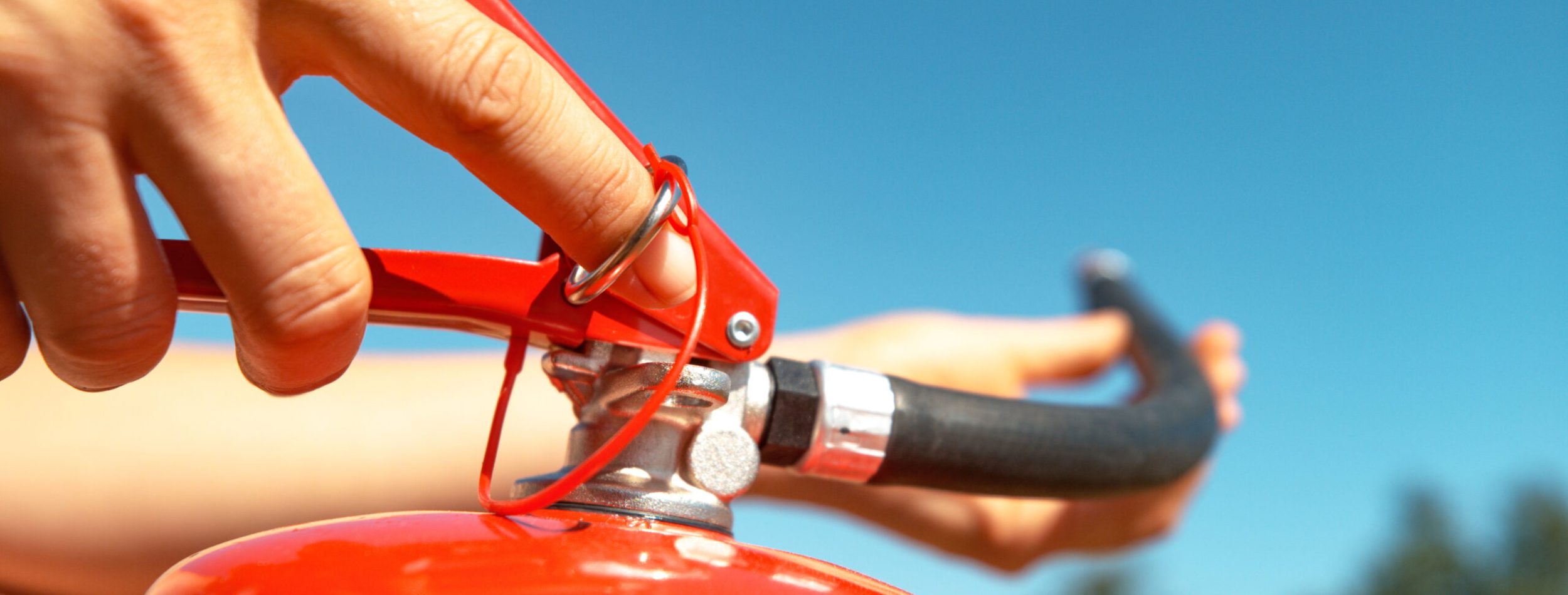 MACRO: Young woman pulls safety pin out of a fire extinguisher b